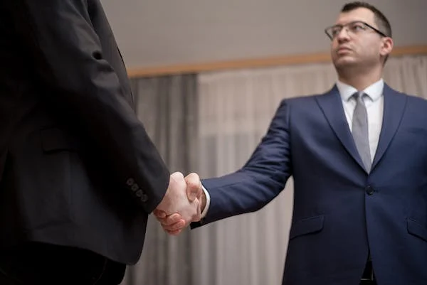 A Person In A Suit Shaking Hands With Another Person In A Suit, Symbolizes The Process Of Bribery